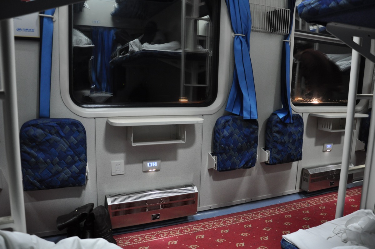 青いカーテンと通路の折りたたみ座席がある、夜の寝台列車の車内