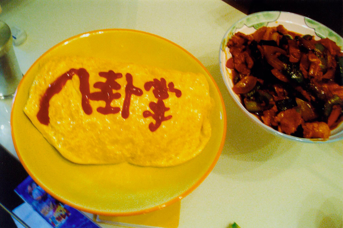 黄色い皿に盛られた、ケチャップで「八卦掌」と描いたオムライスと、隣に並ぶ料理