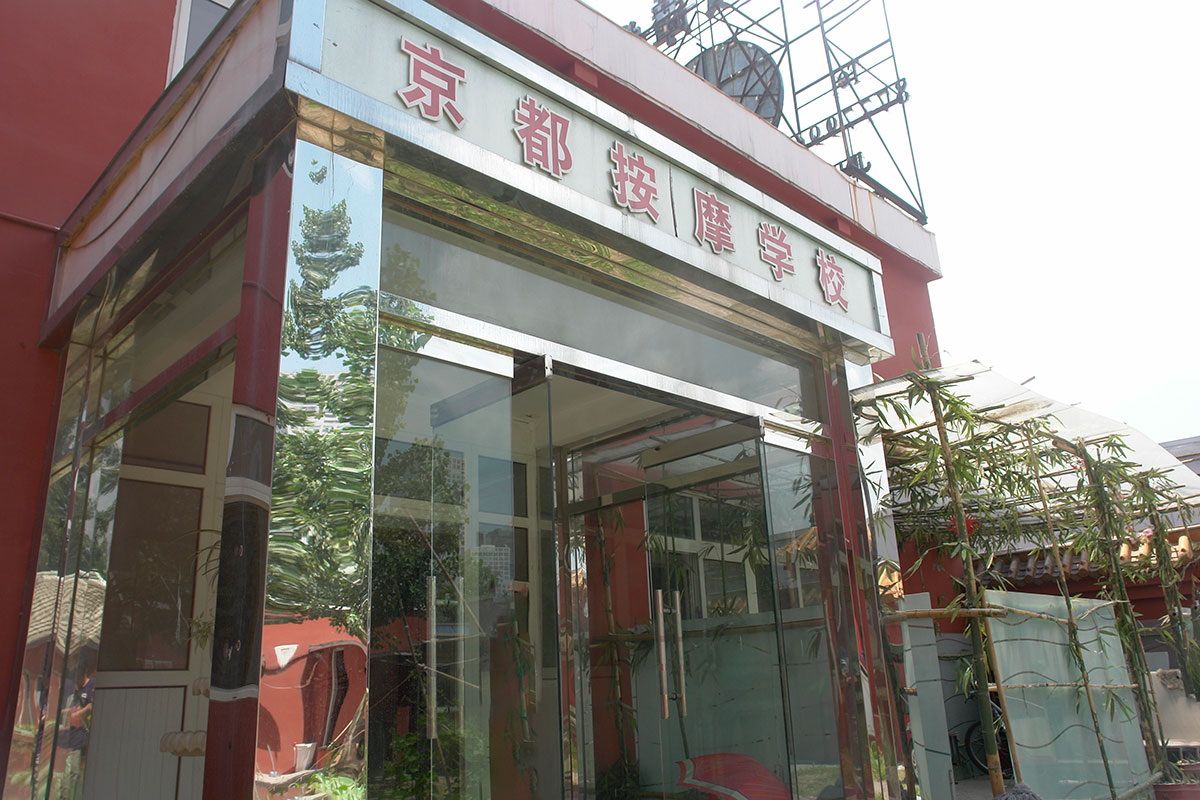 「京都按摩学校」の看板を掲げたガラス張りの入口と、脇に植えられた竹