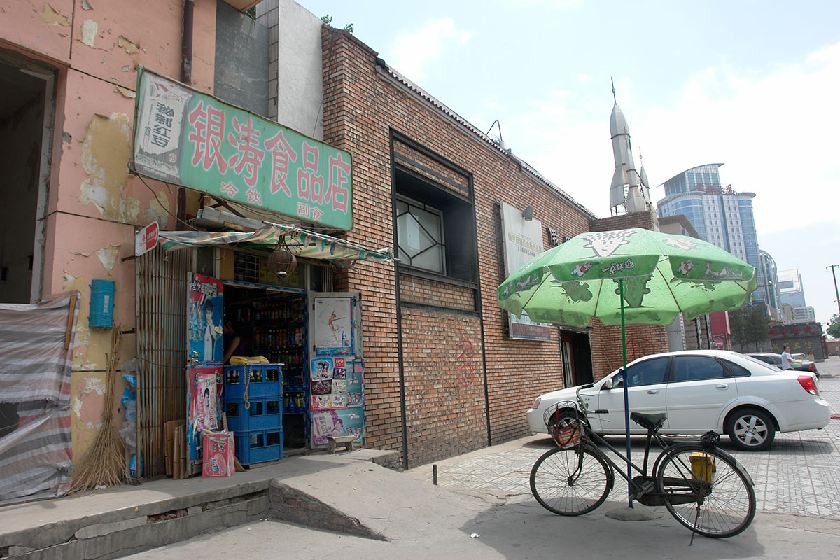 北京の街角にある食品店の入口と、緑のパラソルの下に停められた自転車